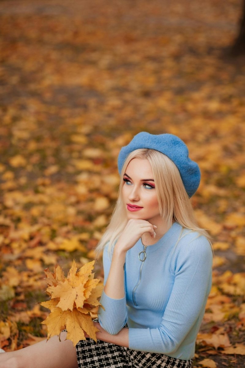 Woman posing in blue dress and beret on autumn leaves